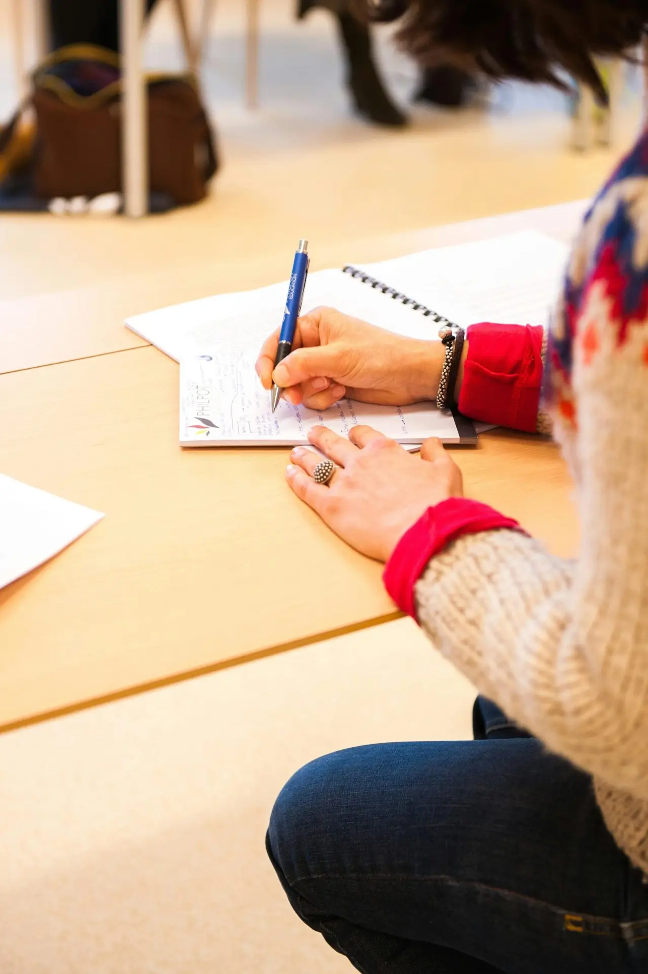 A woman writing notes in a notebook during a classroom lecture setting.